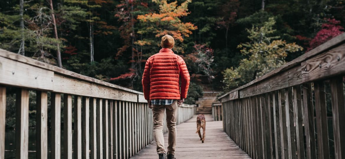 man walking on bridge beside dog during daytime